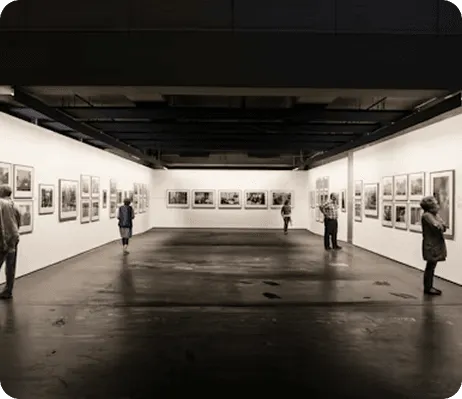 People view framed photographs displayed on white walls in a modern art gallery.