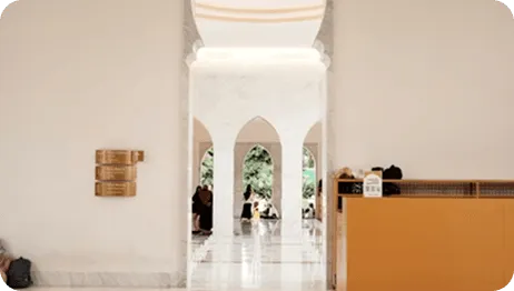 Light-filled interior of a grand hall with arched passages leading to an outdoor garden area.