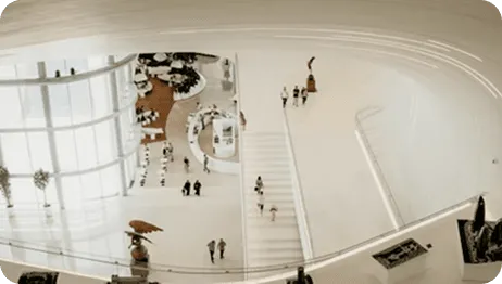 Elevated view of a spacious, modern white museum interior with curving walls and scattered people.
